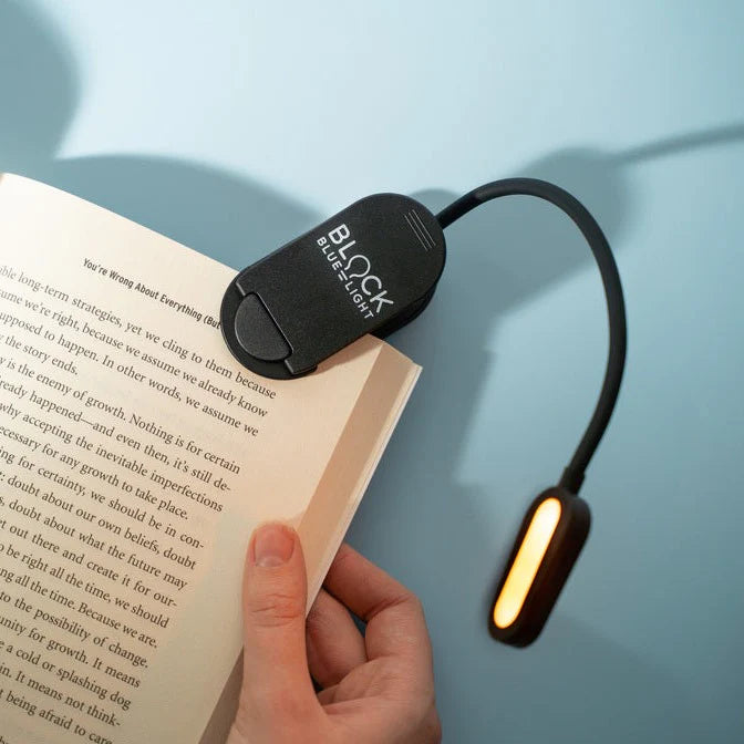 Hand holding a book with a black LED reading light on a blue background