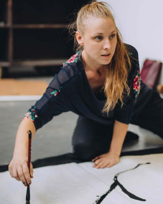 Person drawing on a large sheet of paper with a brush