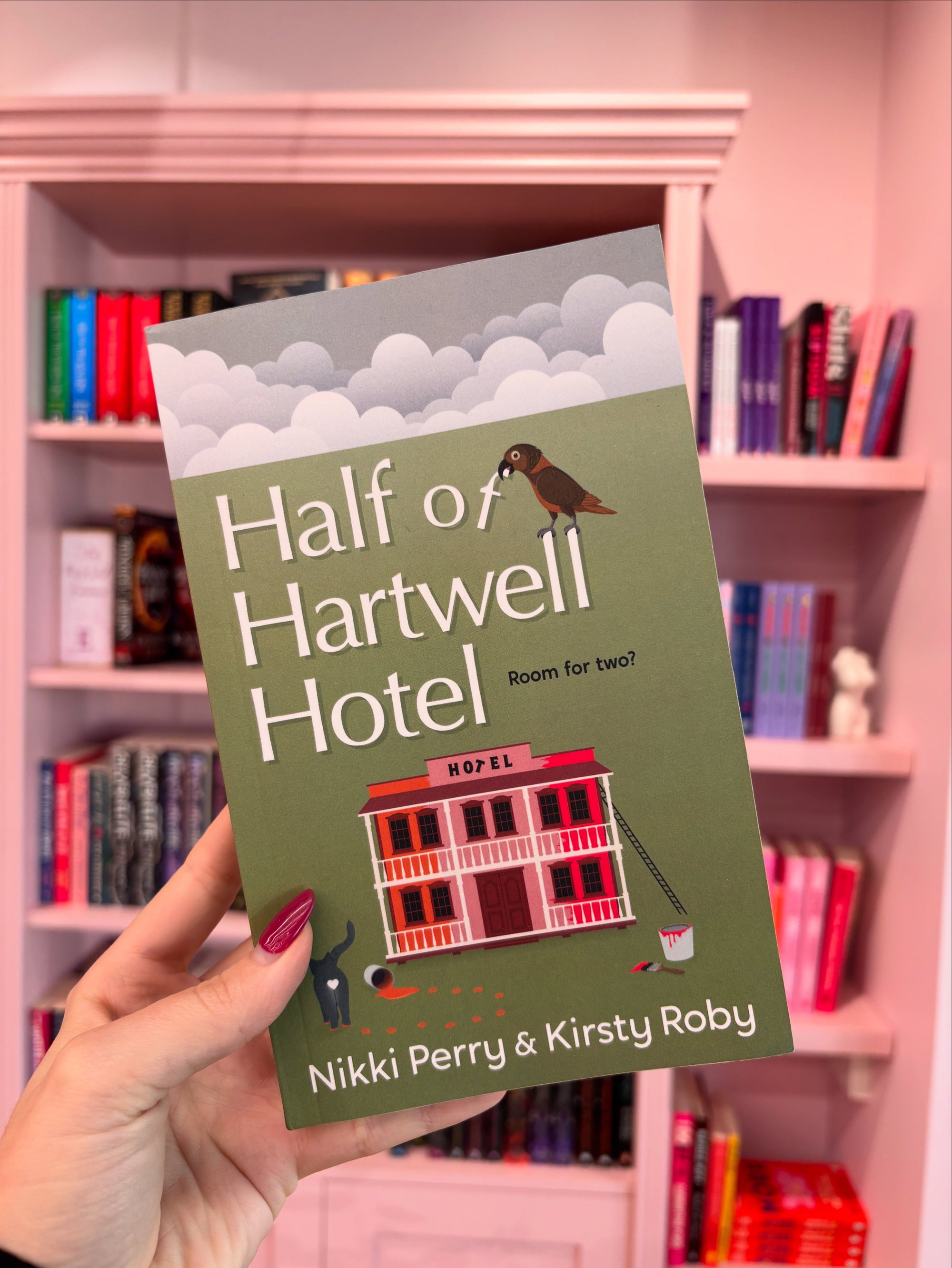 Book titled 'Half of Hartwell Hotel' held in front of a bookshelf.